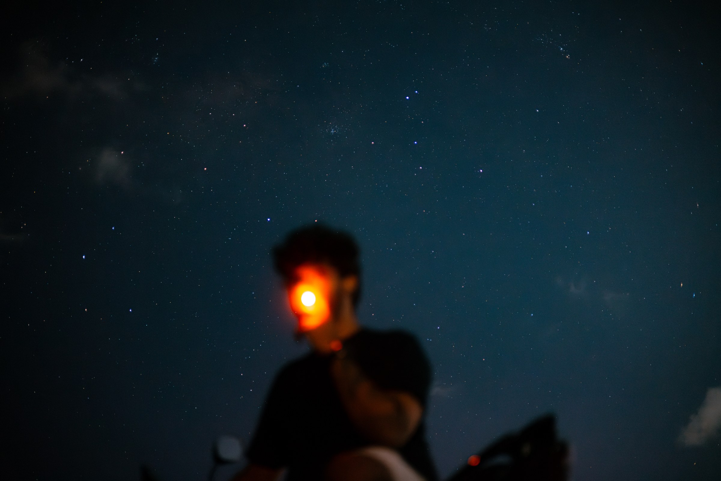 Silhouetted figure on a motorcycle beneath a star-filled night sky, red taillight glowing
