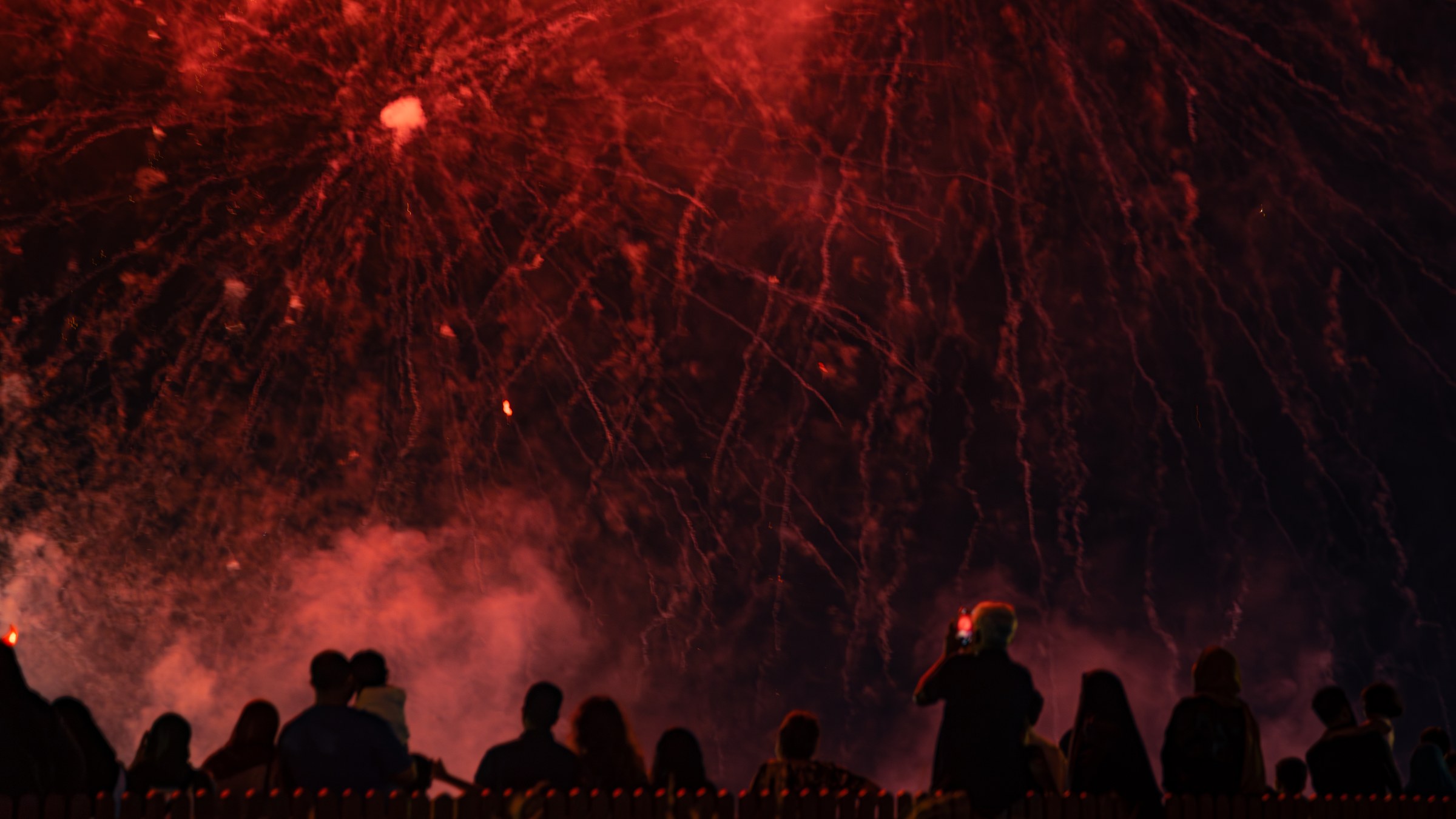 Crowd silhouetted against red fireworks bursting in the night sky