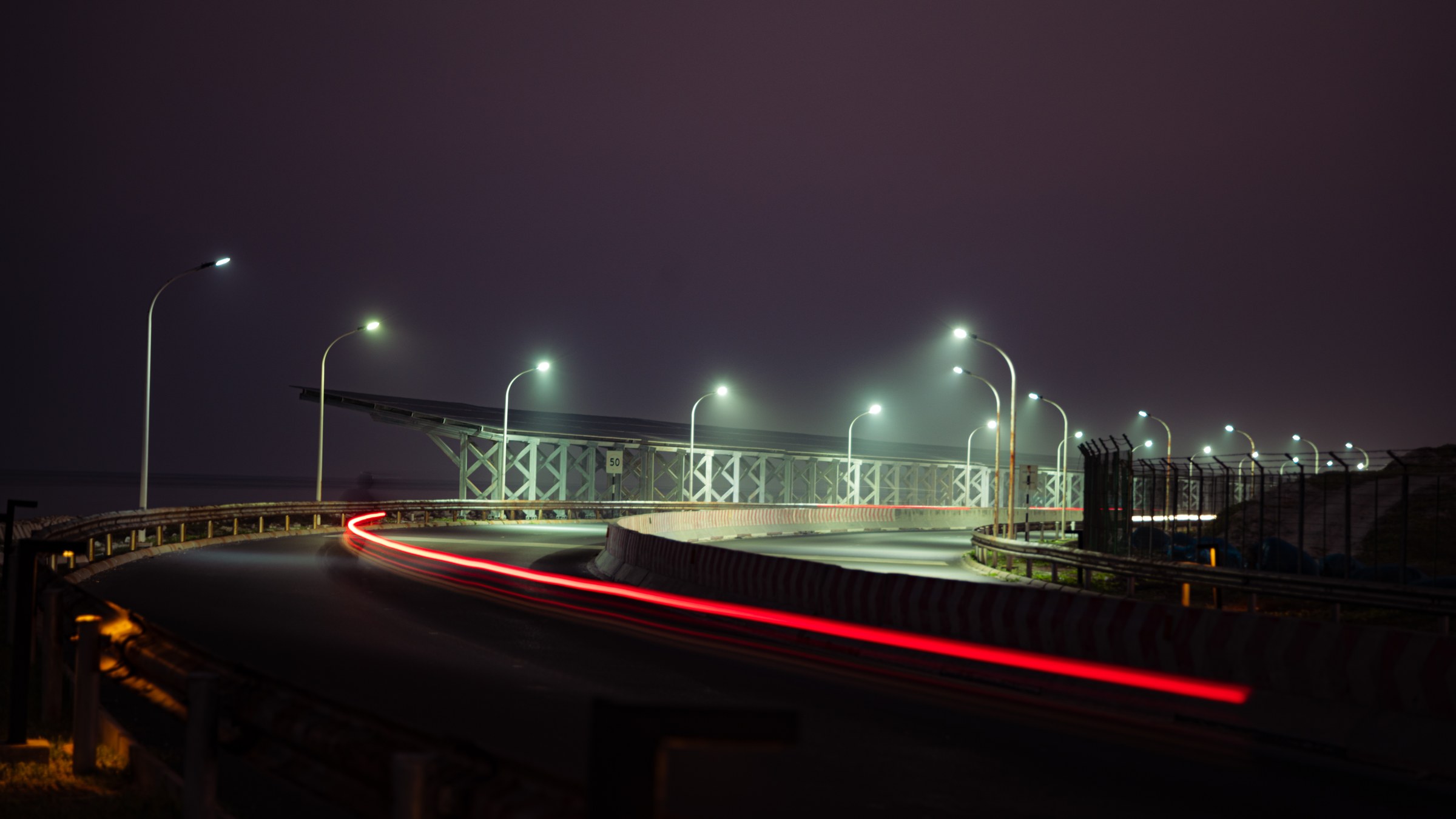Long-exposure night shot of a curved bridge with red light trails and glowing street lamps