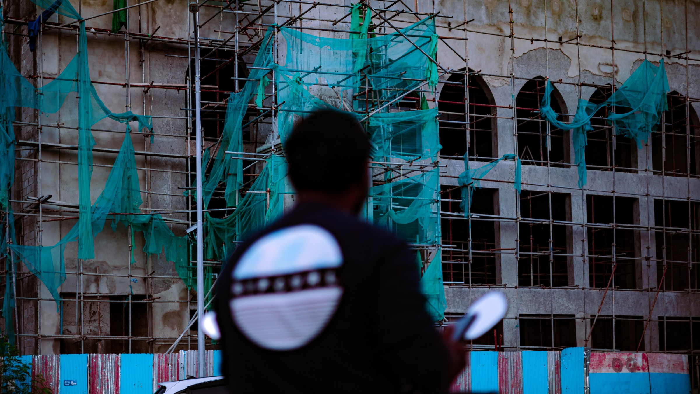 Man facing a building wrapped in green scaffolding nets, back to camera