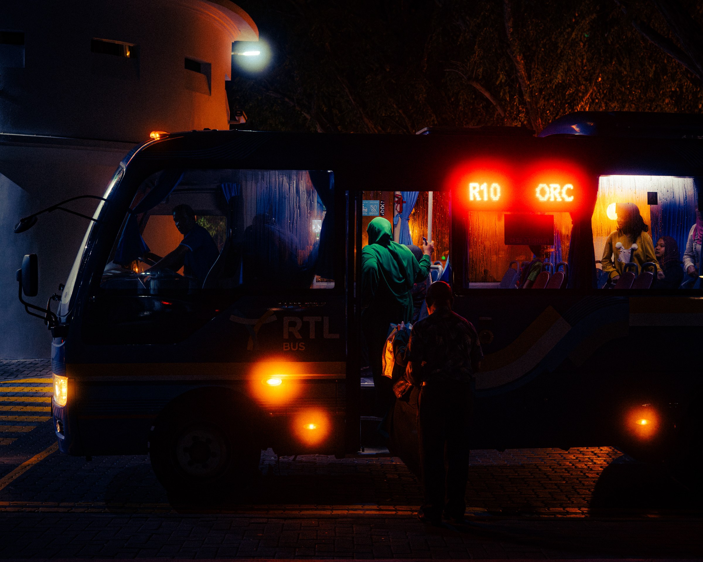 RTL bus at night, orange headlights glowing, passengers visible through lit windows