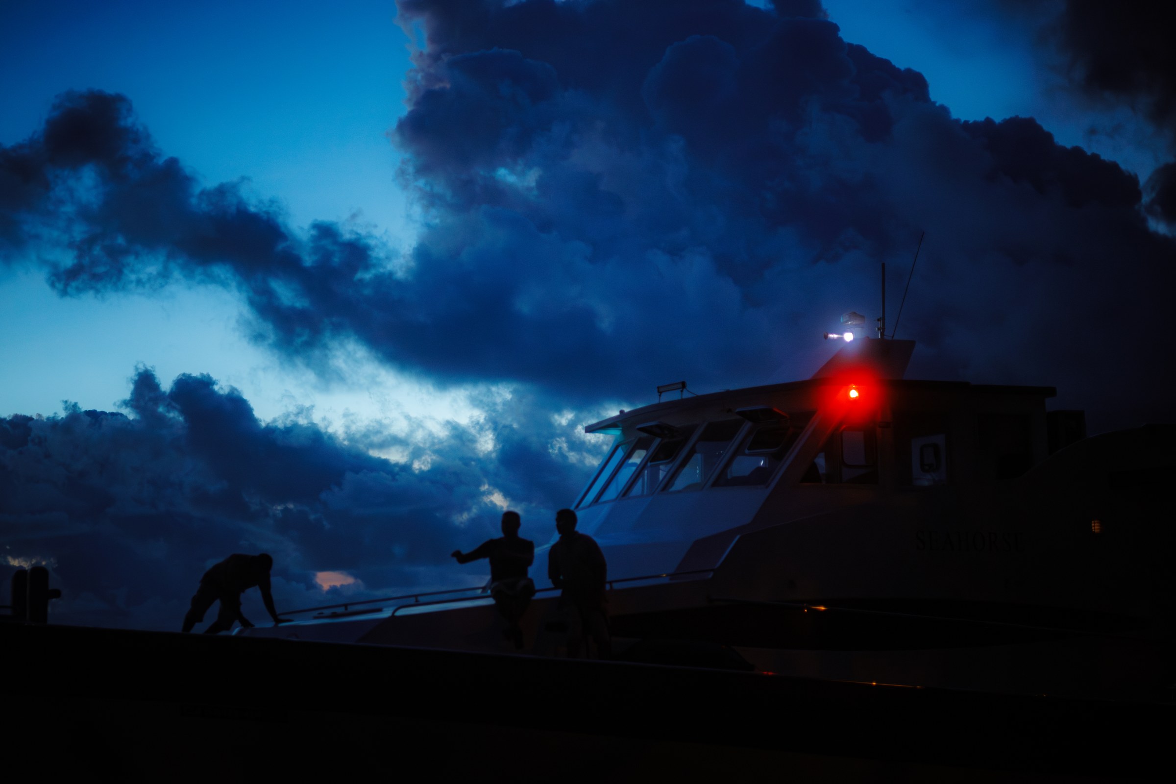 Three figures silhouetted near a ferry at dusk under dramatic storm clouds