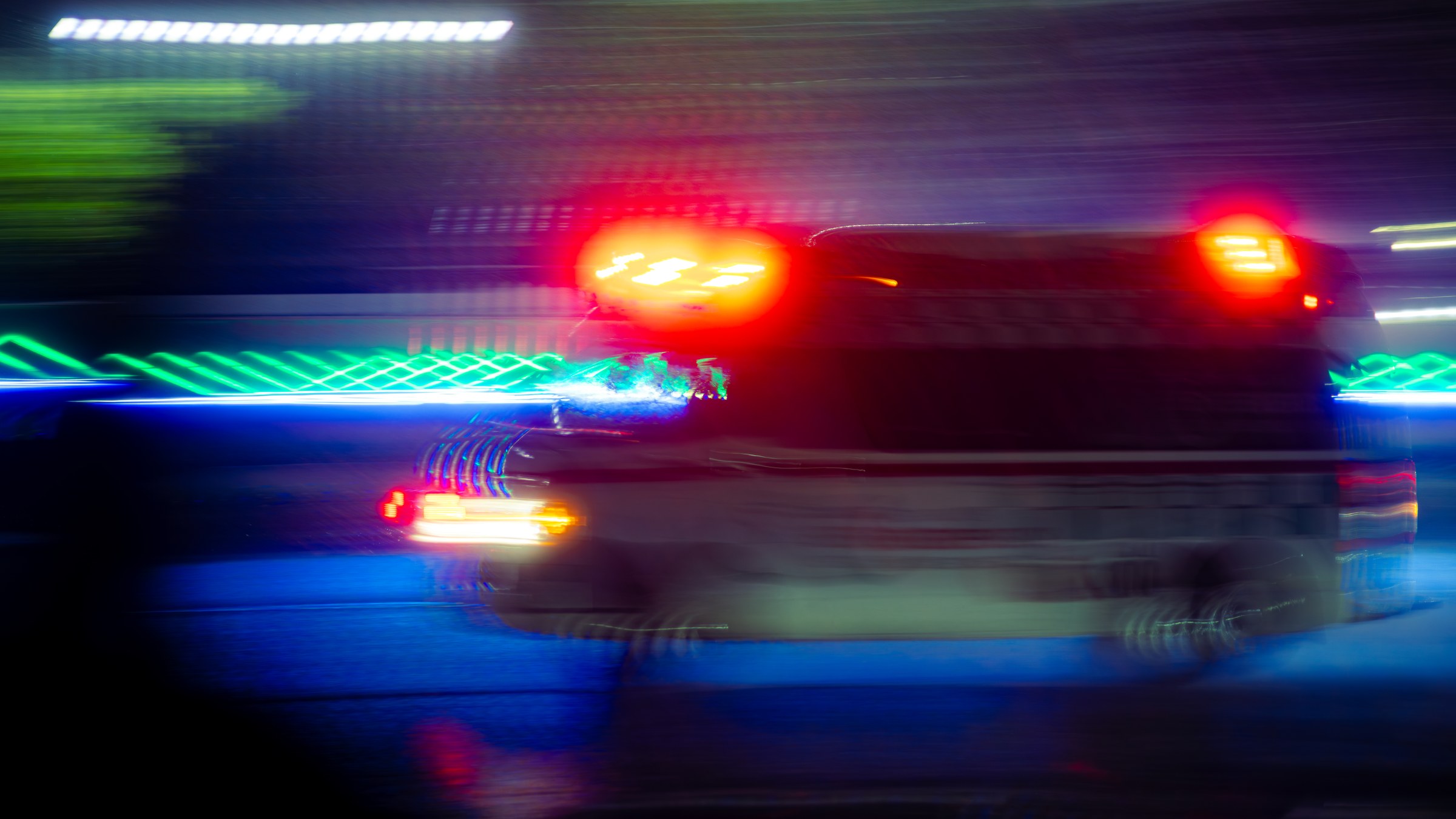 Motion-blurred vehicle surrounded by green and red neon light trails at night