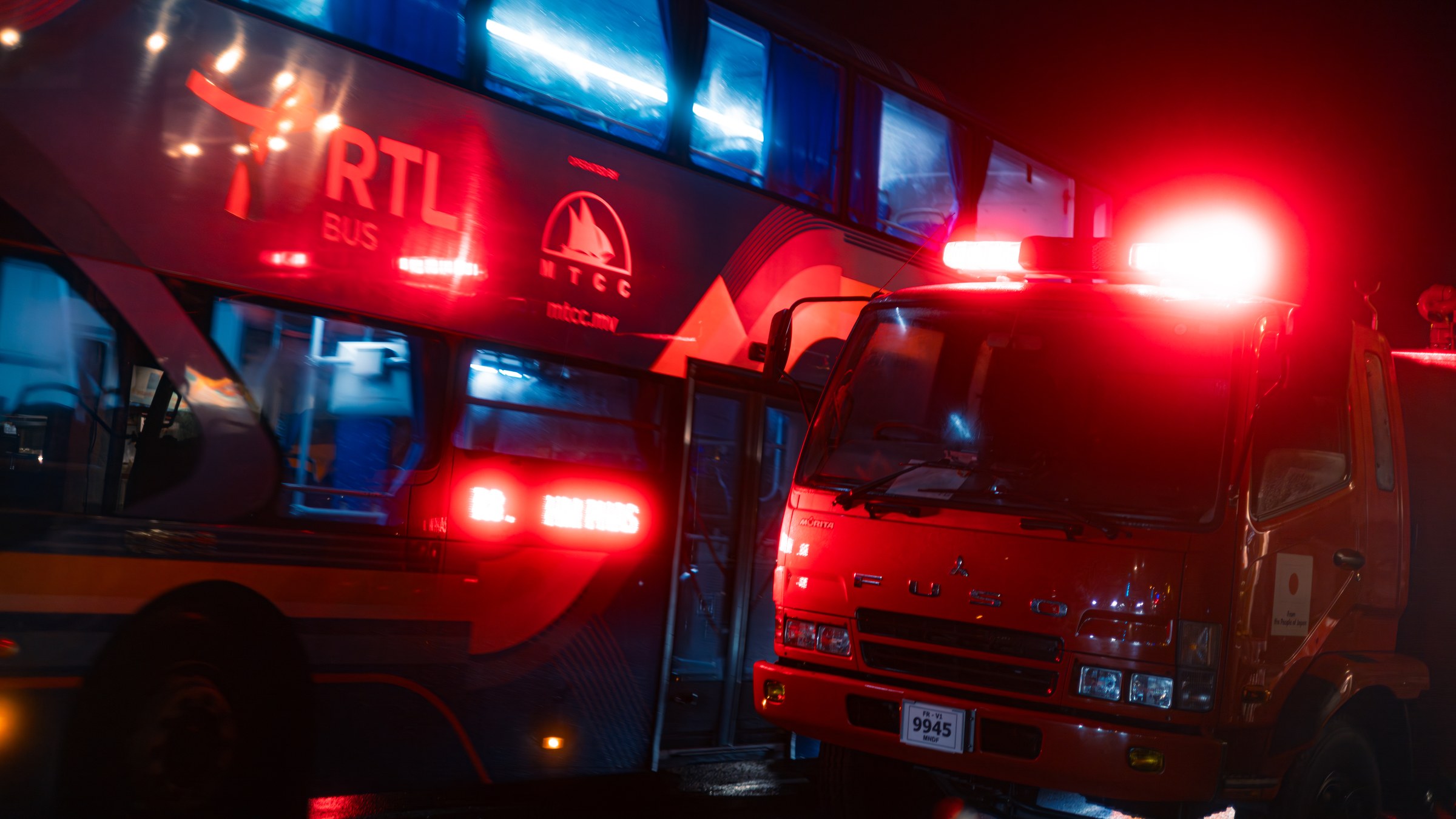 RTL bus beside a red fire truck at night, bathed in emergency lights