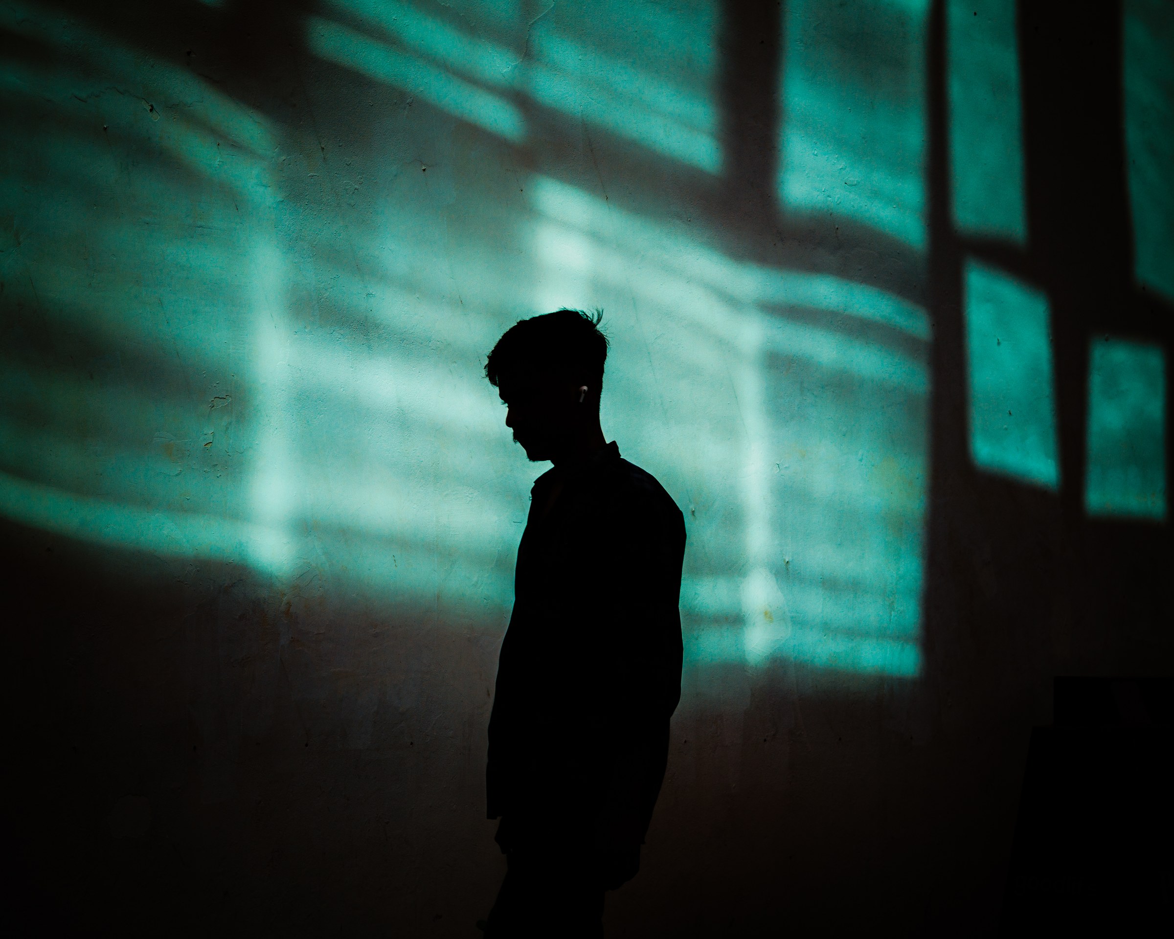 Silhouette of a young man in profile against a wall washed in teal light projections