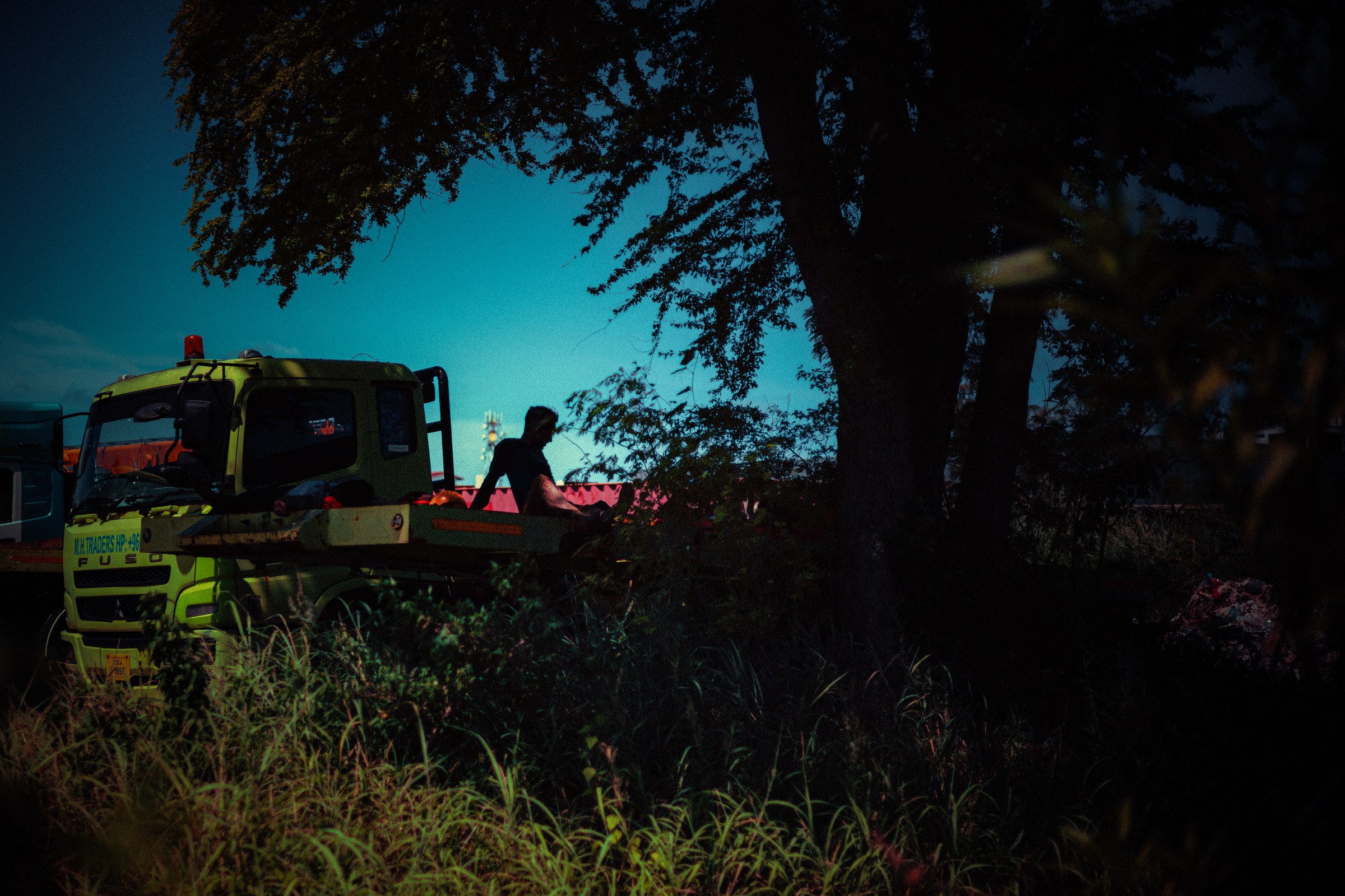Worker silhouetted beside a yellow construction truck at dusk, deep teal sky above