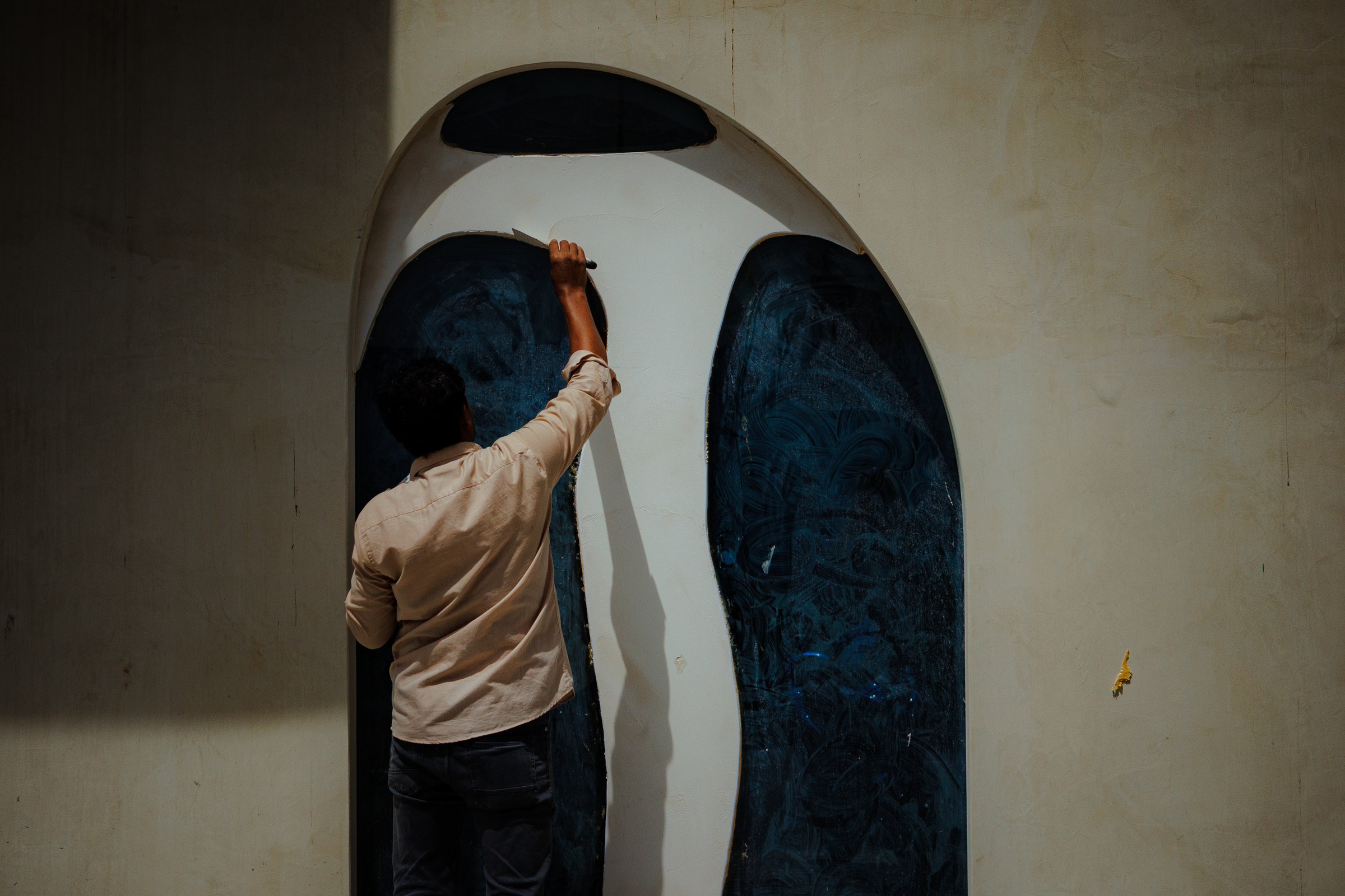 Worker painting a deep blue mural inside an arched doorway, back to camera in warm side light