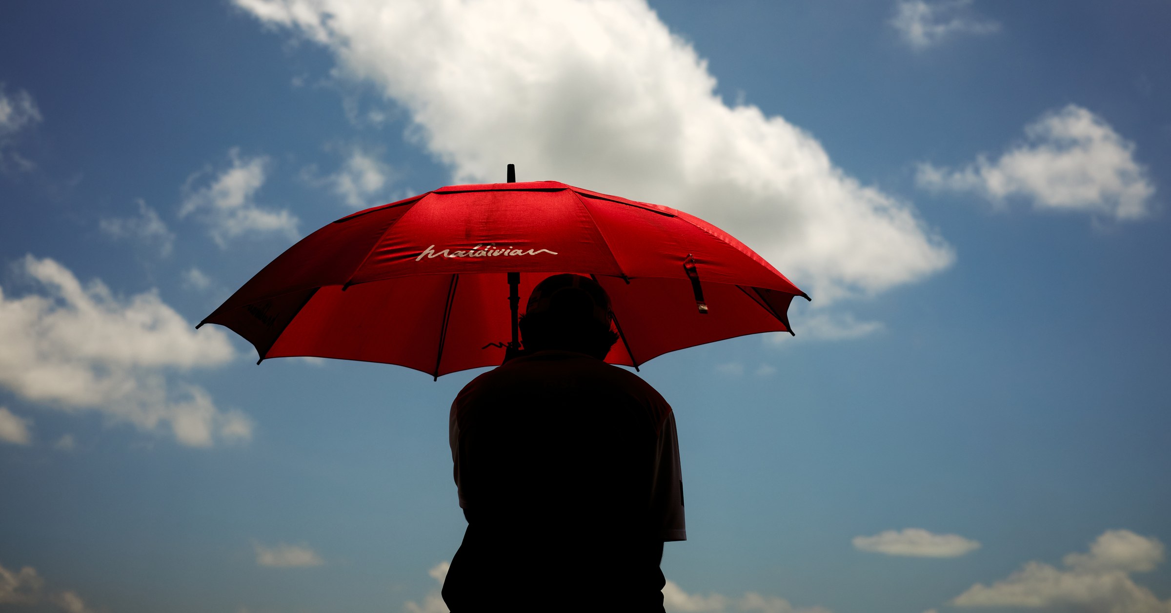 Silhouette of a man holding a large red Maldivian umbrella against a bright clouded sky