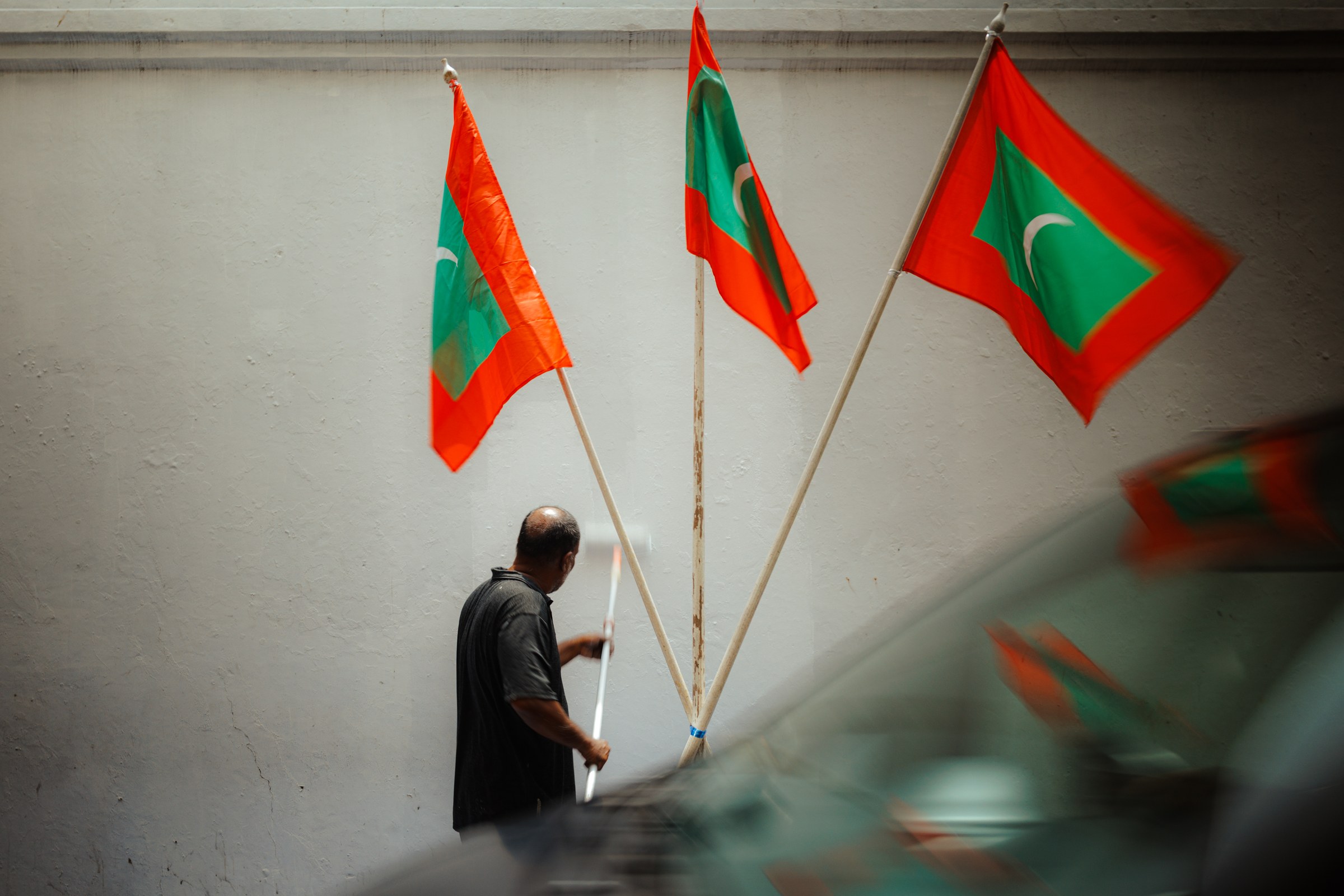 Man bundling three Maldivian national flags against a pale wall