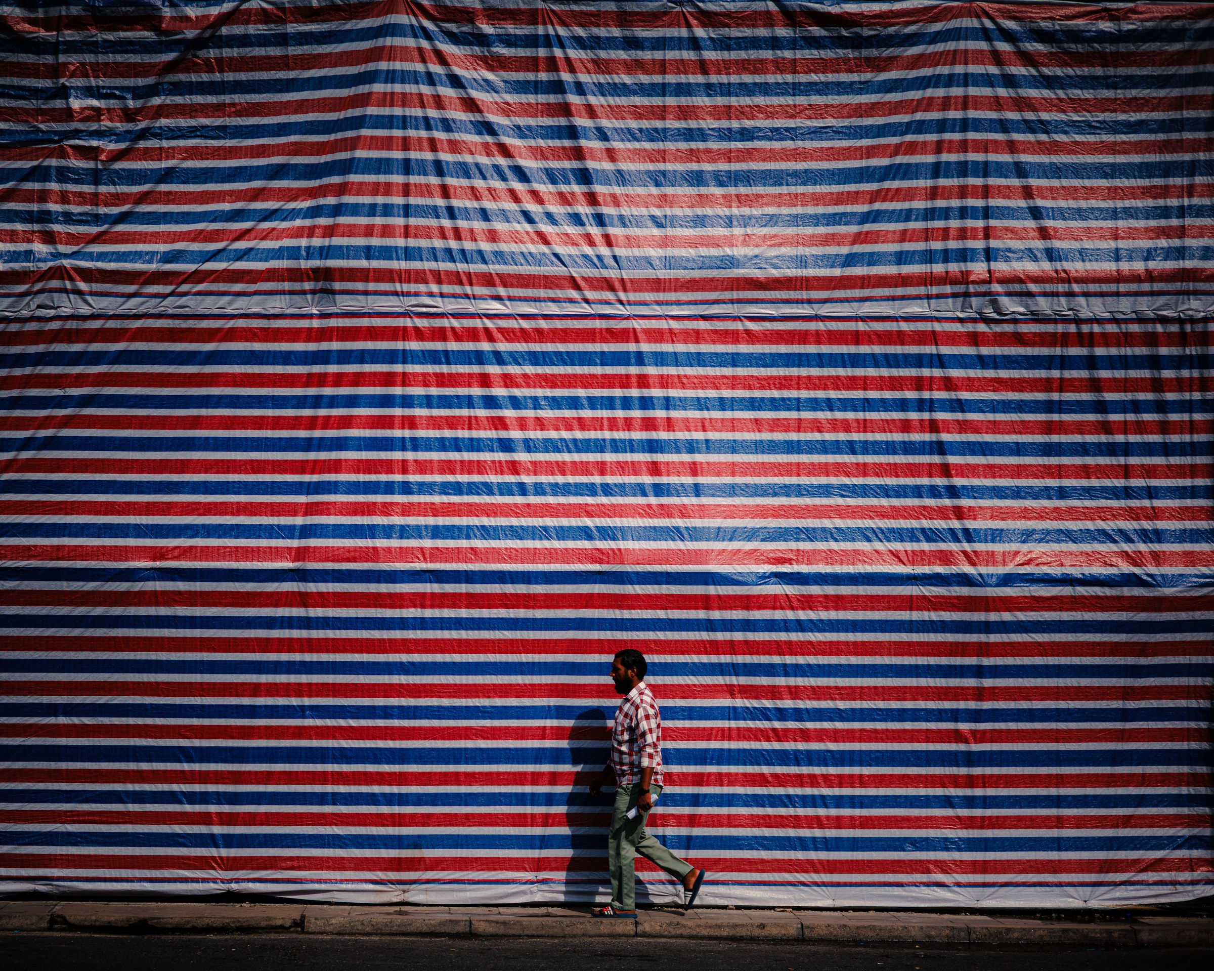 Man walking in front of a massive red and blue striped tarpaulin wall
