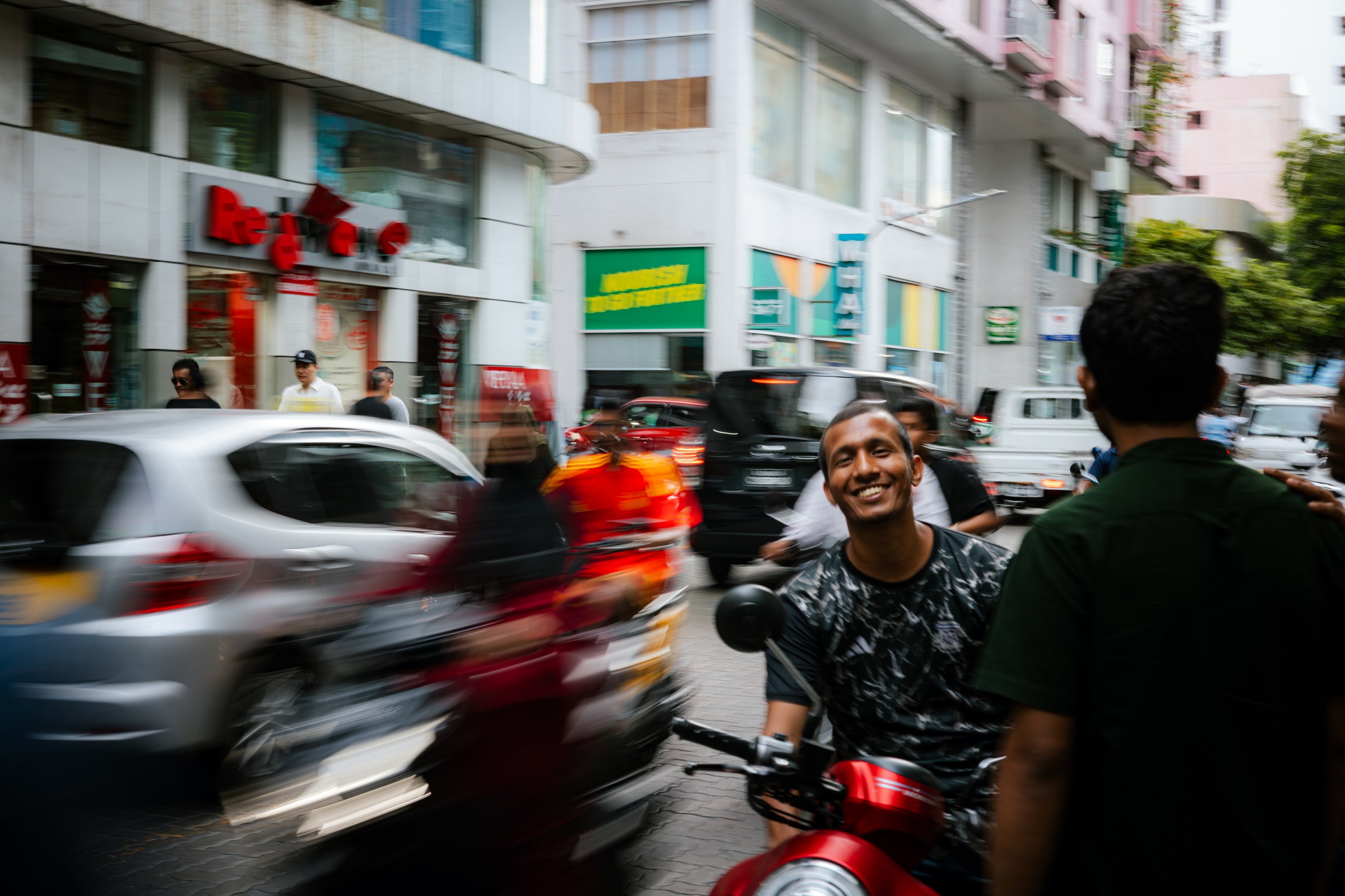 Young man grinning on a scooter in the blur of a busy Malé street