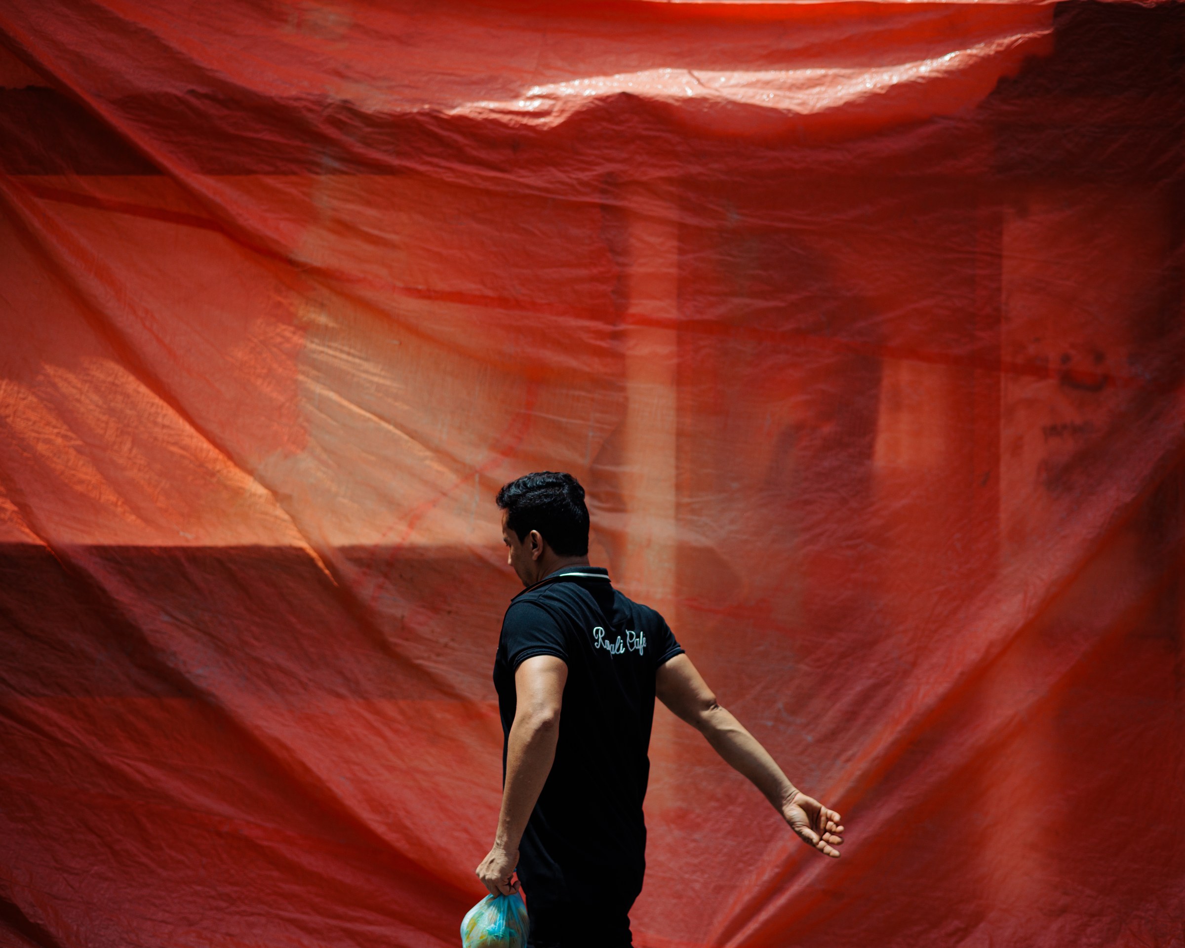 Man in a black shirt walking in front of a wide orange-red tarpaulin wall