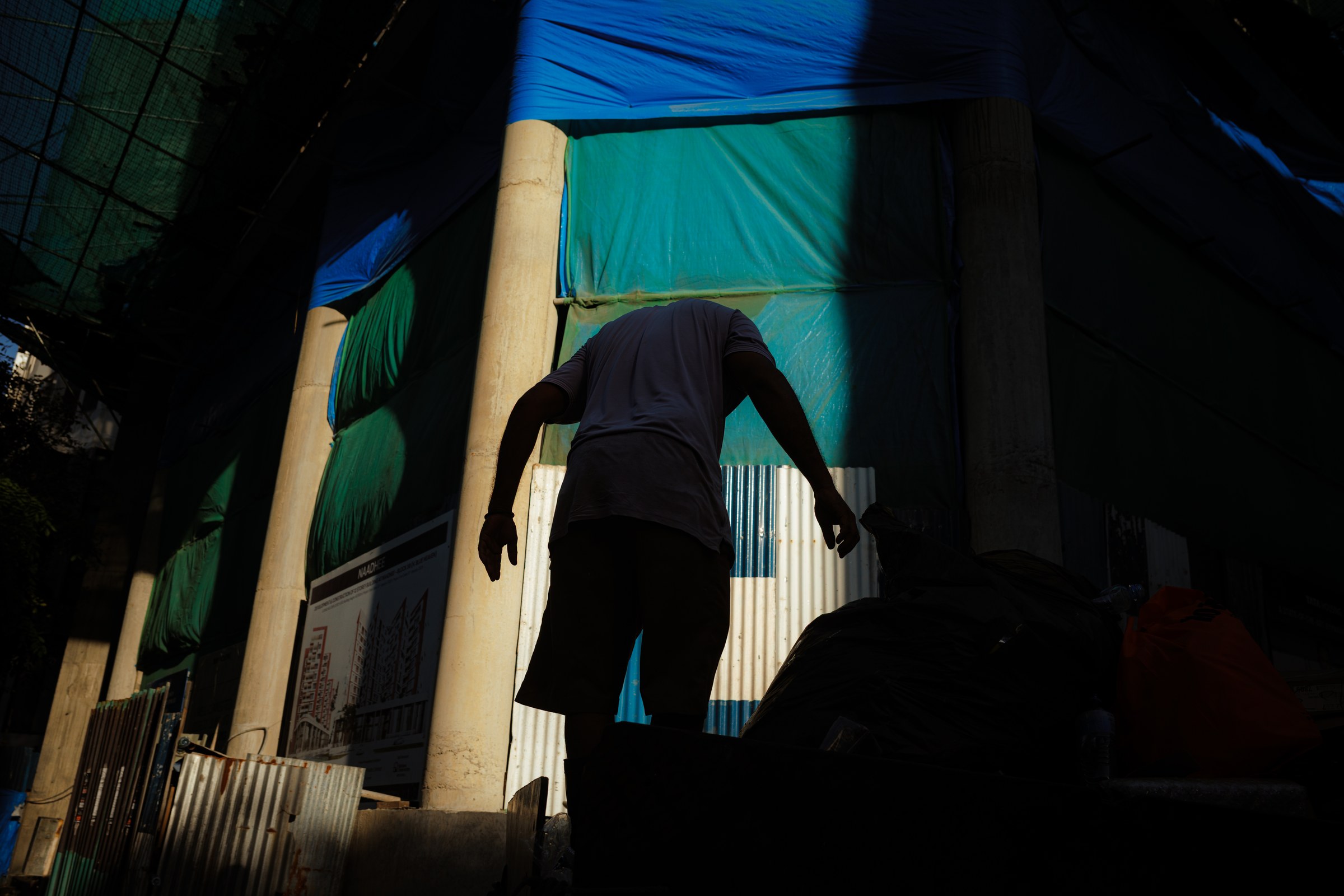 Worker's silhouette stepping through a gap in a construction site, blue and teal tarpaulins above
