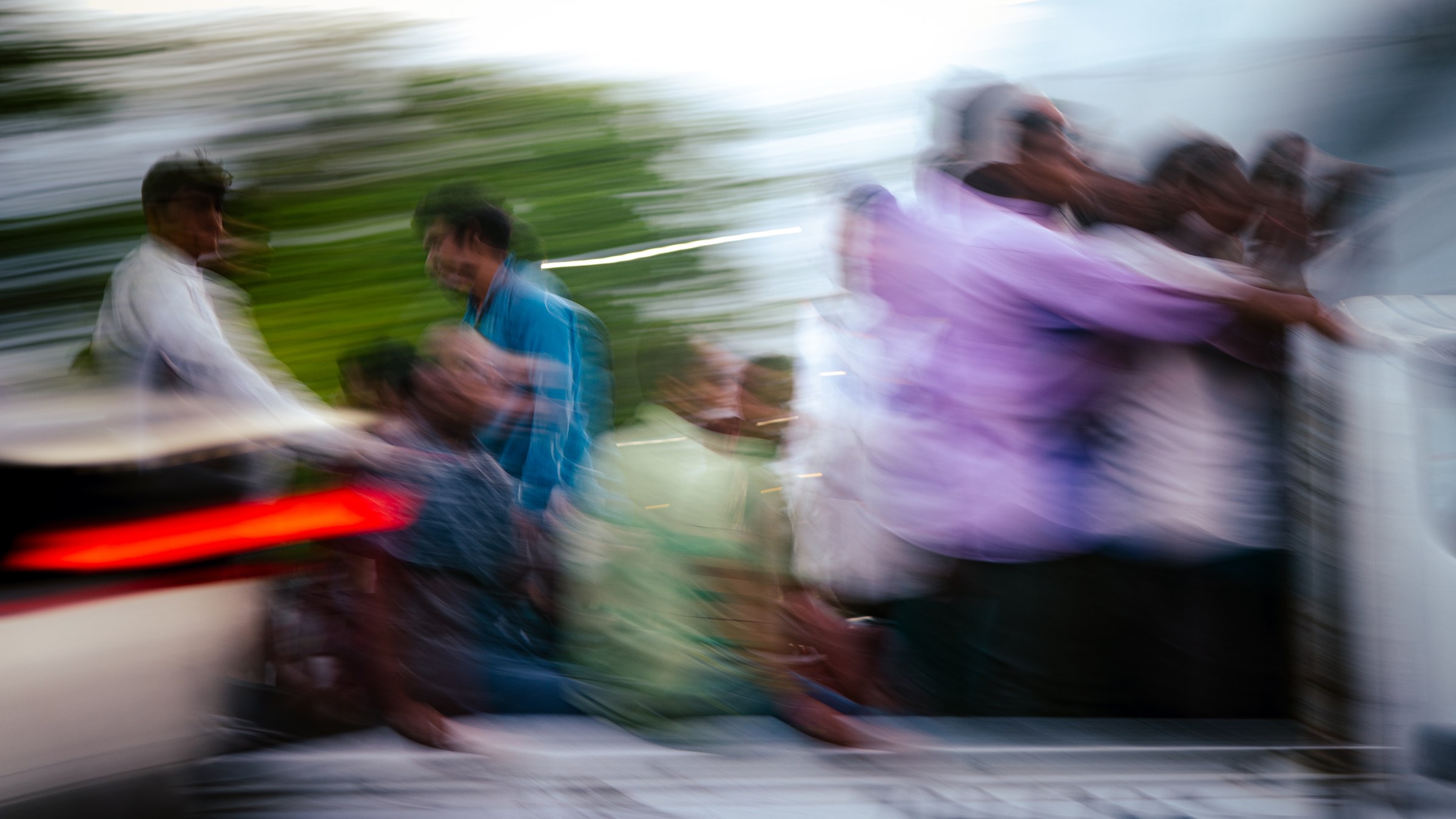 Group of people in motion blur on a moving vehicle, blue and purple tones, trees streaking behind